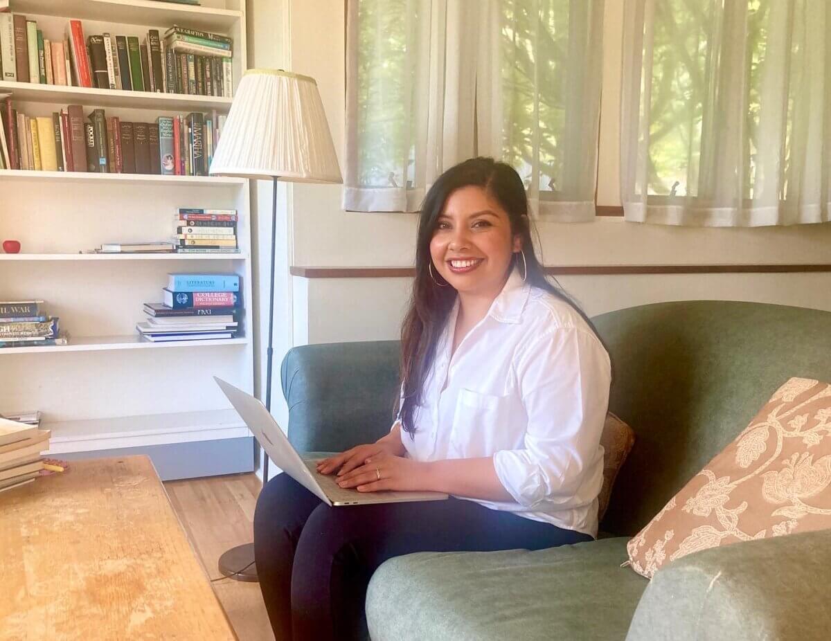 Maria Alvarez sitting on a couch with an open laptop on her lap in her Saltonstall studio