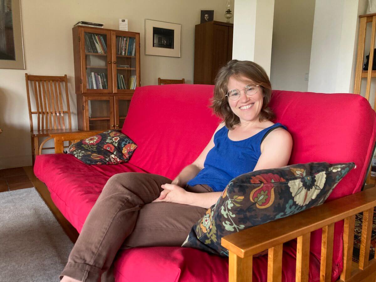 writer Helen Rubinstein sits smiling on a red futon couch in the Saltonstall living room
