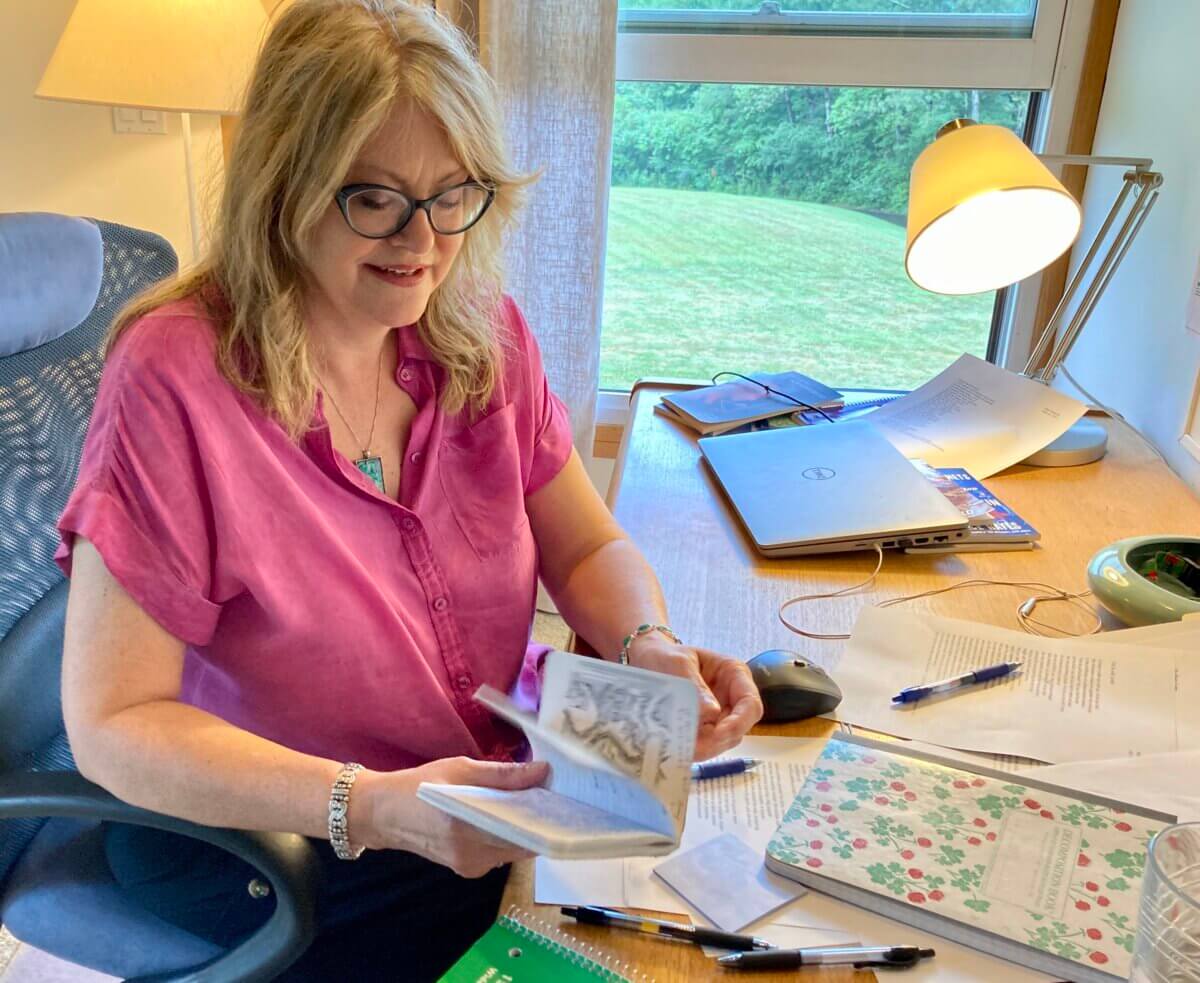 poet Amy Lemmon sitting at her desk at Saltonstall with journals and notes spread out in front of her