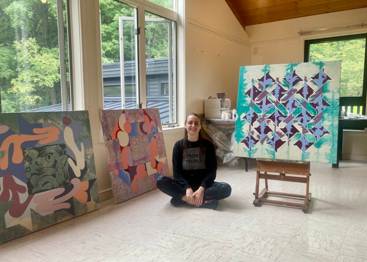 artist Debbi Kenote sits on her Saltonstall studio floor in front of three new colorful abstract paintings