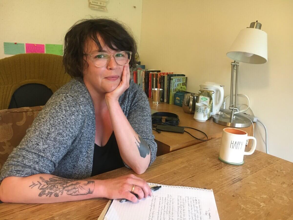 writer E.C. Barrett sitting at her Saltonstall desk with her chin in her hand and drafts in front of her