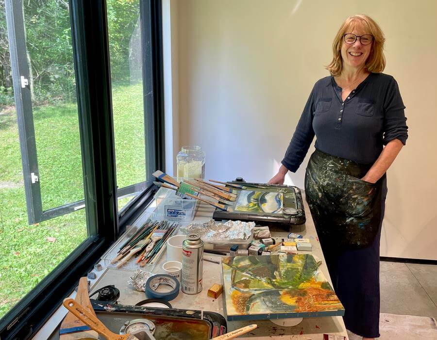 Grace Kim, smiling, sitting at a desk filled with colored pencils and a large work-in-progress